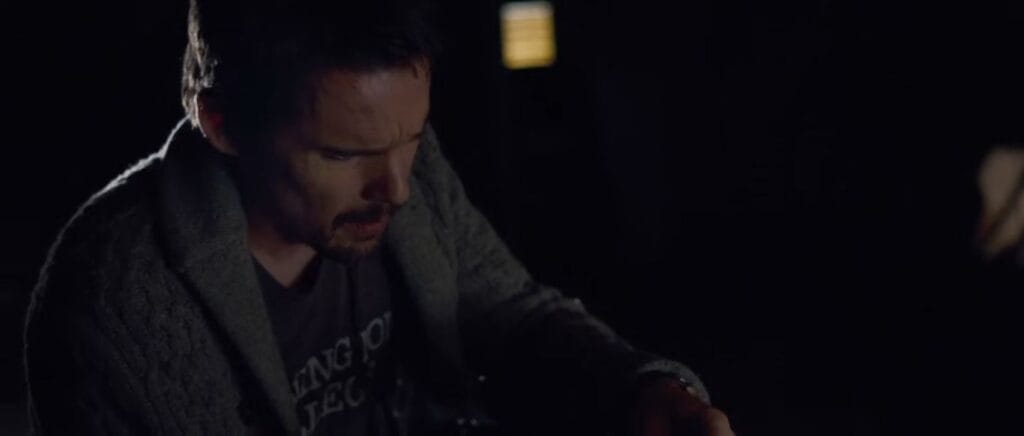 Ethan Hawke as Ellison Oswalt looking down anxiously with a furrowed brow in dim lighting in Sinister.