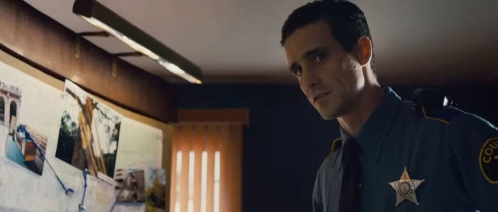 James Ransone as Deputy So & So standing inside an office looking intrigued in Sinister.
