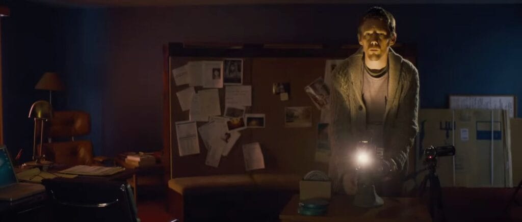 Ellison Oswalt standing over a bright film projector in his dark home office in Sinister.
