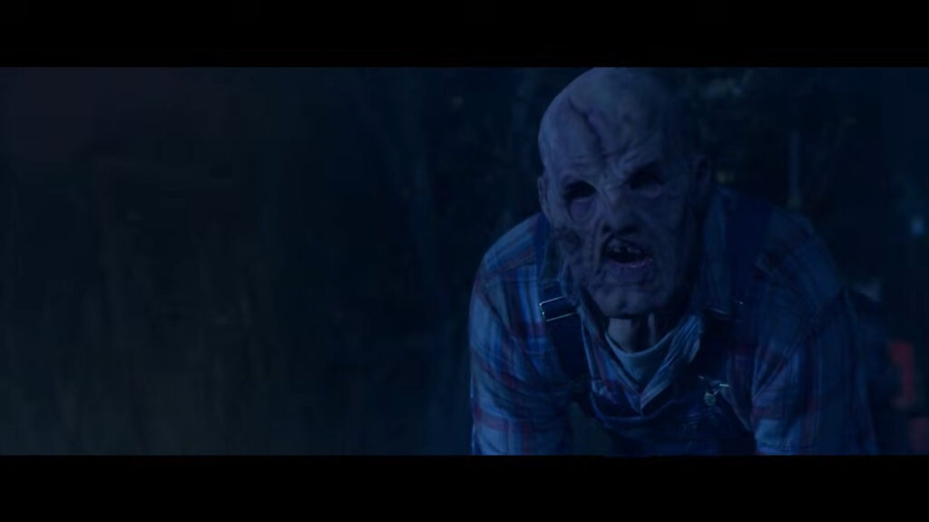 A disfigured, hulking slasher wearing overalls and a flannel shirt in the dark during the Friday the 31st segment of Tales of Halloween.