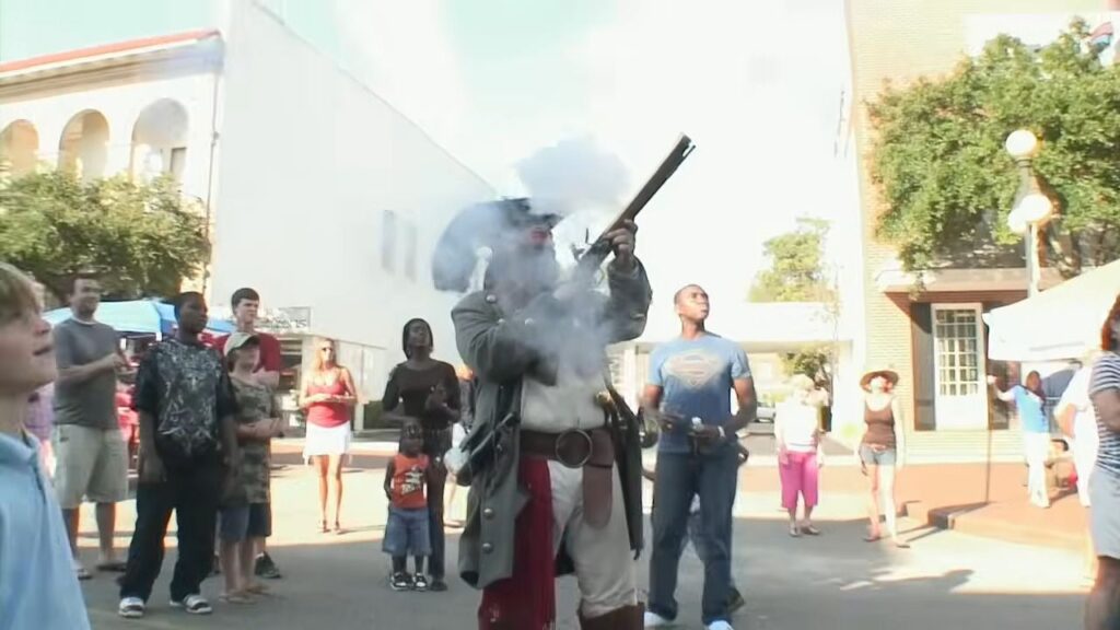 A man dressed in historic colonial attire firing a musket during a parade in The Bay.