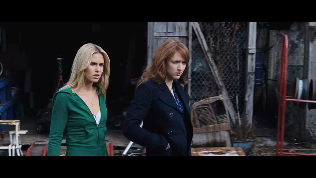 Anna Hutchison as Jules and Kristen Connolly as Dana looking anxious outside a rustic workshop in The Cabin in the Woods.