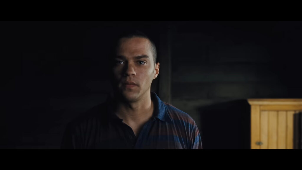 Jesse Williams as Holden looking forward with a serious expression in a dimly lit room in The Cabin in the Woods.