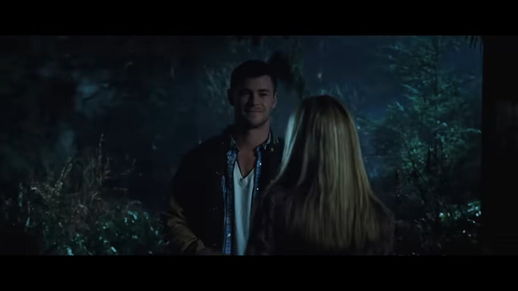 Chris Hemsworth as Curt smiling while talking to Jules in the dark woods in The Cabin in the Woods.