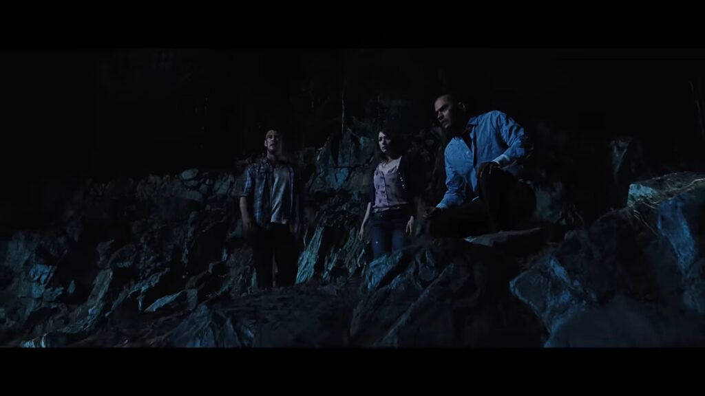 Marty, Dana, and Holden standing on a rocky outcrop at night looking upward in The Cabin in the Woods.