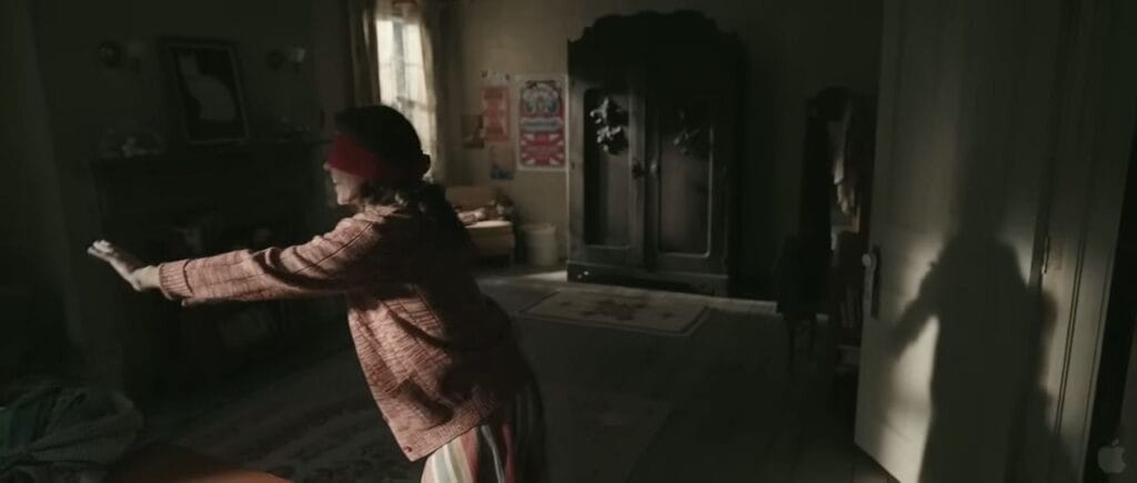 Lili Taylor as Carolyn blindfolded playing hide-and-clap with outstretched arms in a dim room in The Conjuring.