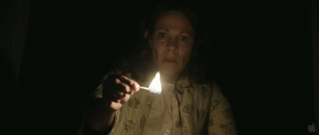 Carolyn Perron holding a lit match with a terrified expression in pitch darkness in The Conjuring.