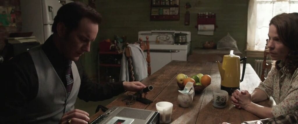 Patrick Wilson as Ed Warren operating a reel tape recorder while interviewing a distressed Carolyn Perron in The Conjuring.