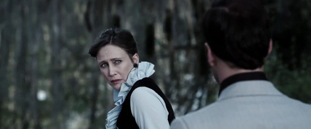 Vera Farmiga as Lorraine Warren looking back over her shoulder with an uneasy expression outdoors in The Conjuring.