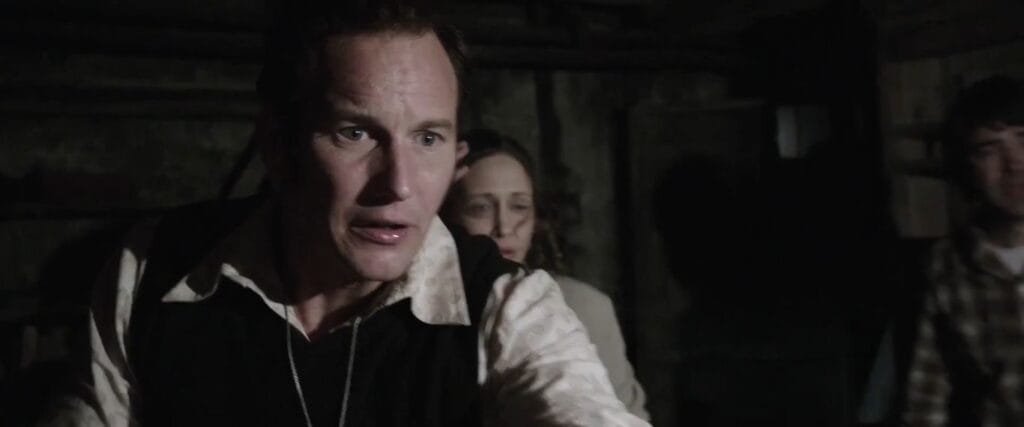 Ed Warren shouting anxiously with a flashlight alongside Lorraine in a dark basement in The Conjuring.