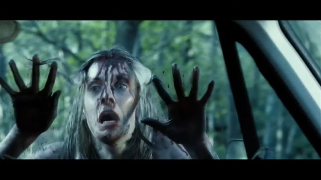 A bloodied and frantic Shauna Macdonald as Sarah pressing her hands against a car window in The Descent: Part 2.