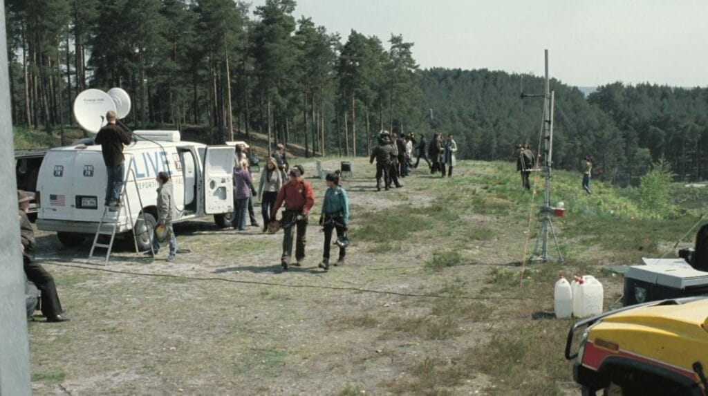 Emergency vehicles, news vans, and search-and-rescue teams gathering in a cleared wooded area in The Descent: Part 2.