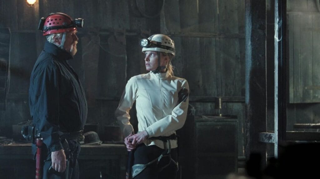 Two rescue team members in caving gear and headlamps talking inside a dim mine building in The Descent: Part 2.