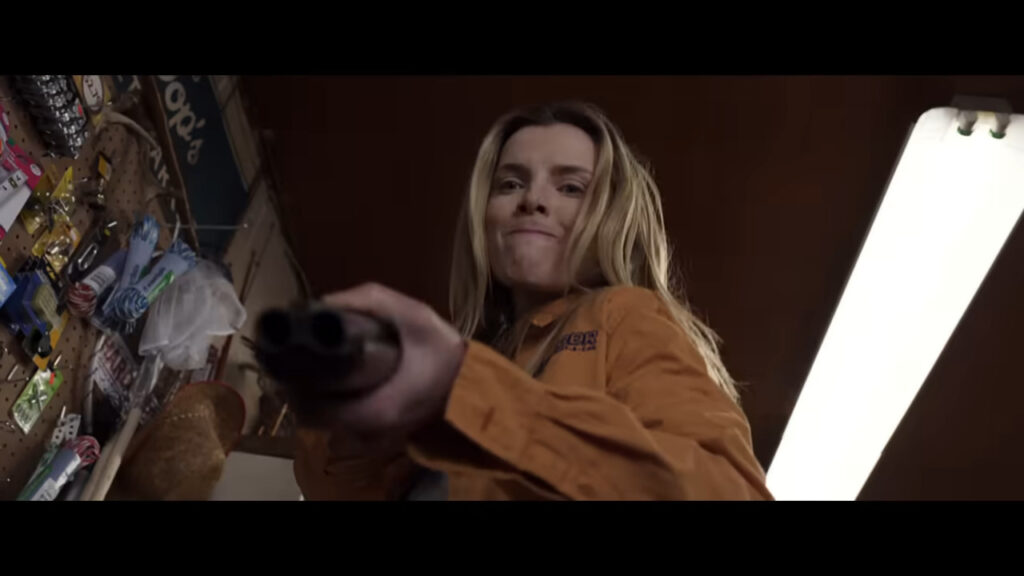 Betty Gilpin as Crystal aiming a double-barrel shotgun forward with a fierce, determined expression in The Hunt.