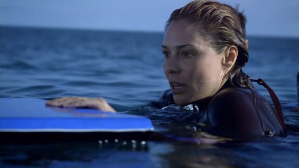 Zoe Naylor as Kate clinging to a flotation board and looking panicked while swimming in open water in The Reef.