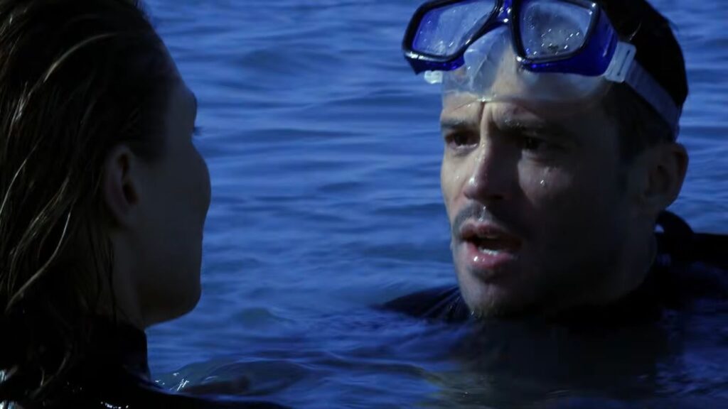 Damian Walshe-Howling as Luke wearing a dive mask and speaking tensely to Kate while treading water in The Reef.