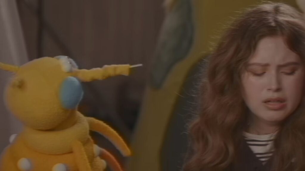 A young woman looking distressed beside a yellow Jim Henson puppet in V/H/S/Mixtape.