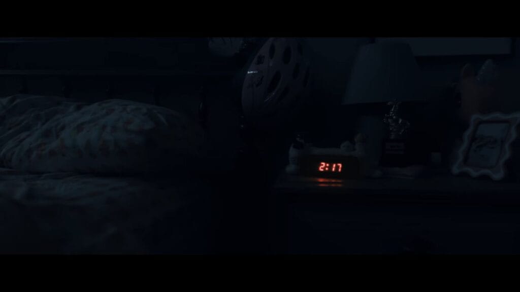 A digital alarm clock glowing 2:17 in red numbers in a dark, empty bedroom in Weapons.