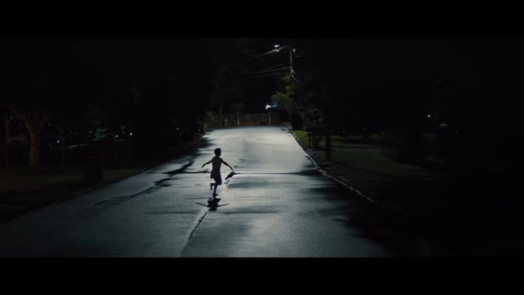 A silhouette of a child running down the center of an empty suburban street at night under a streetlight in Weapons.