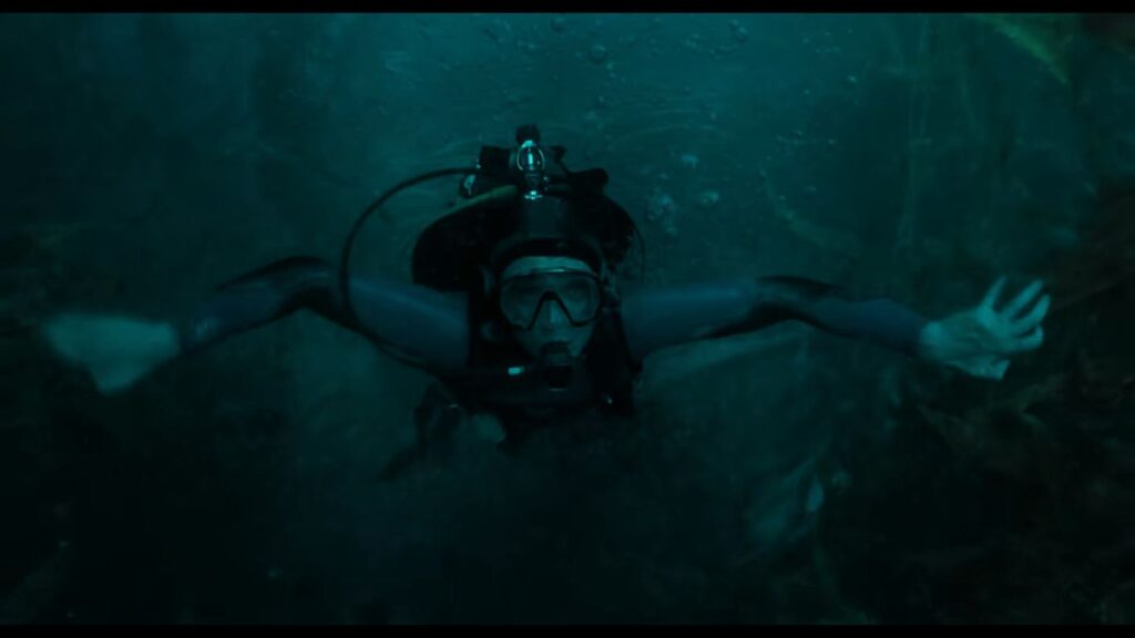 Austin Abrams as Jay Gardiner scuba diving with outstretched arms in deep, murky green water in Whalefall.