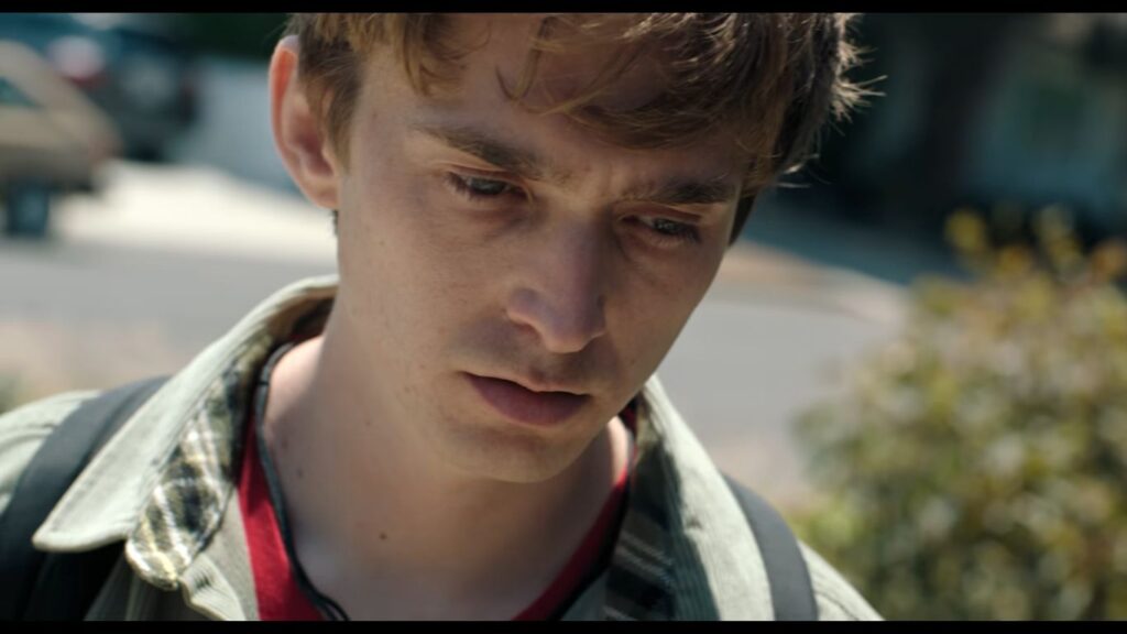 Austin Abrams looking downward with a sombre and troubled expression in Whalefall.
