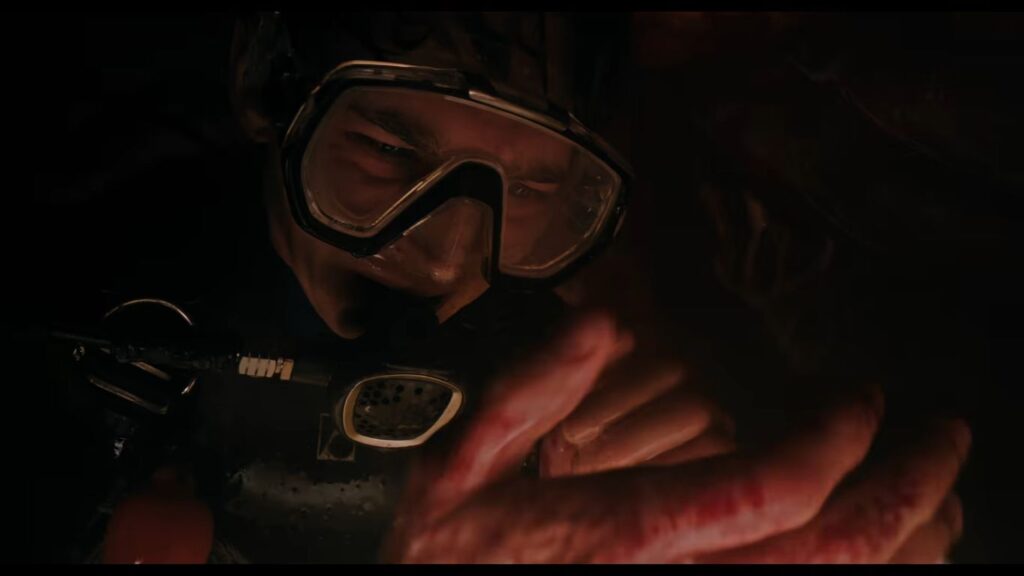 Jay wearing a scuba mask and looking distressed in pitch darkness while examining his bloody hand inside the whale in Whalefall.