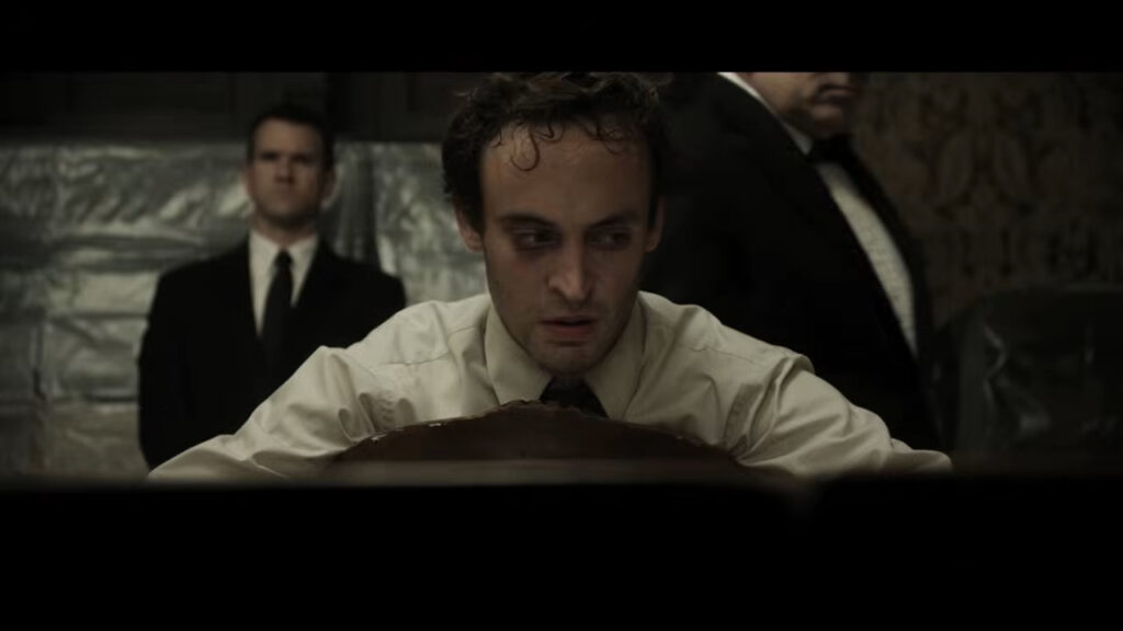 A distressed contestant leaning forward over a chair with guards standing behind him in Would You Rather.