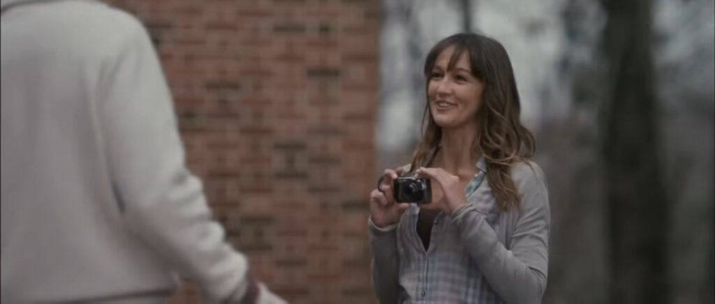 Sharni Vinson as Erin smiling outdoors holding a digital camera in You're Next.