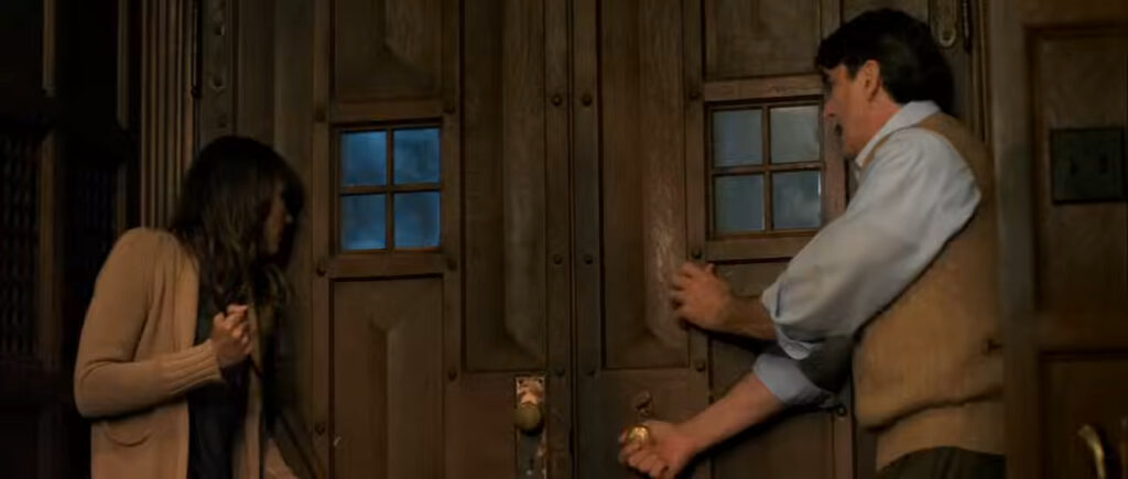 Erin and Paul anxiously trying to secure and lock the heavy wooden front doors in You're Next.
