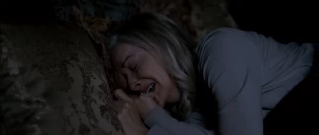 Kelly lying in bed crying in terror while burying her face into a pillow in You're Next.